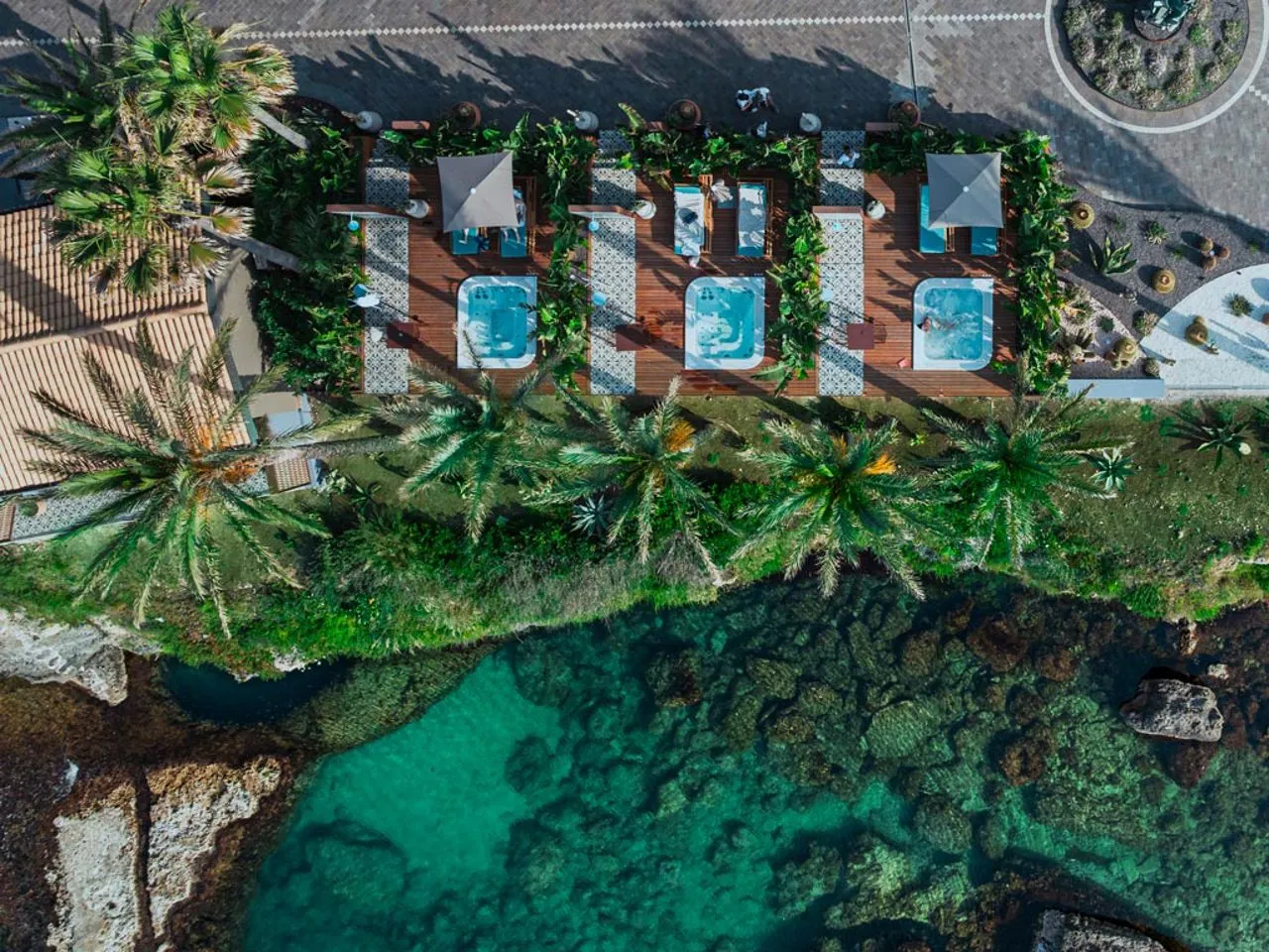 Veduta aerea di vasche idromassaggio su terrazza in legno tra palme sul mare