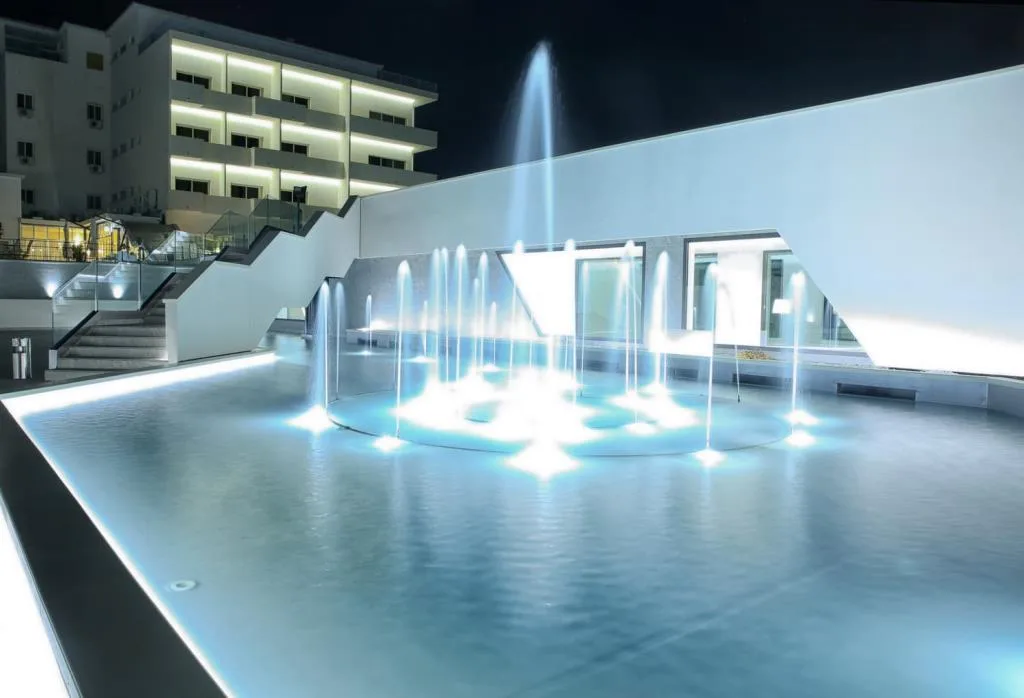 Fontana illuminata di notte con giochi d'acqua e hotel sullo sfondo