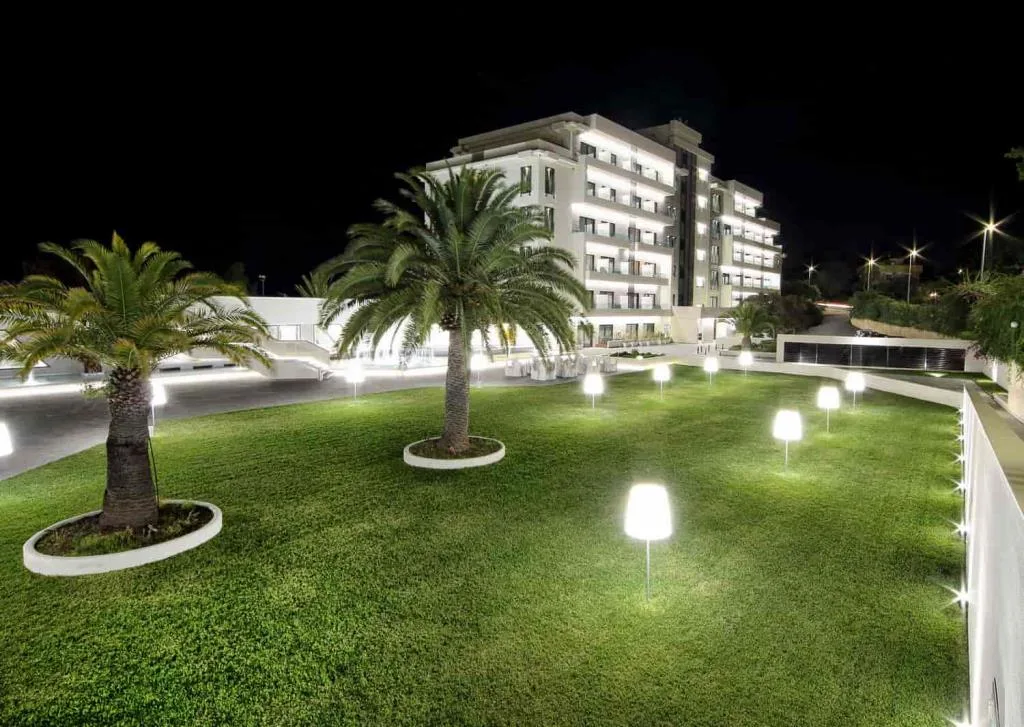 Giardino notturno dell'hotel con palme, prato e lampade luminose