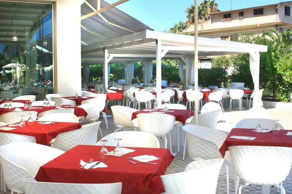Terrazza ristorante coperta con tavoli dalle tovaglie rosse e sedie bianche