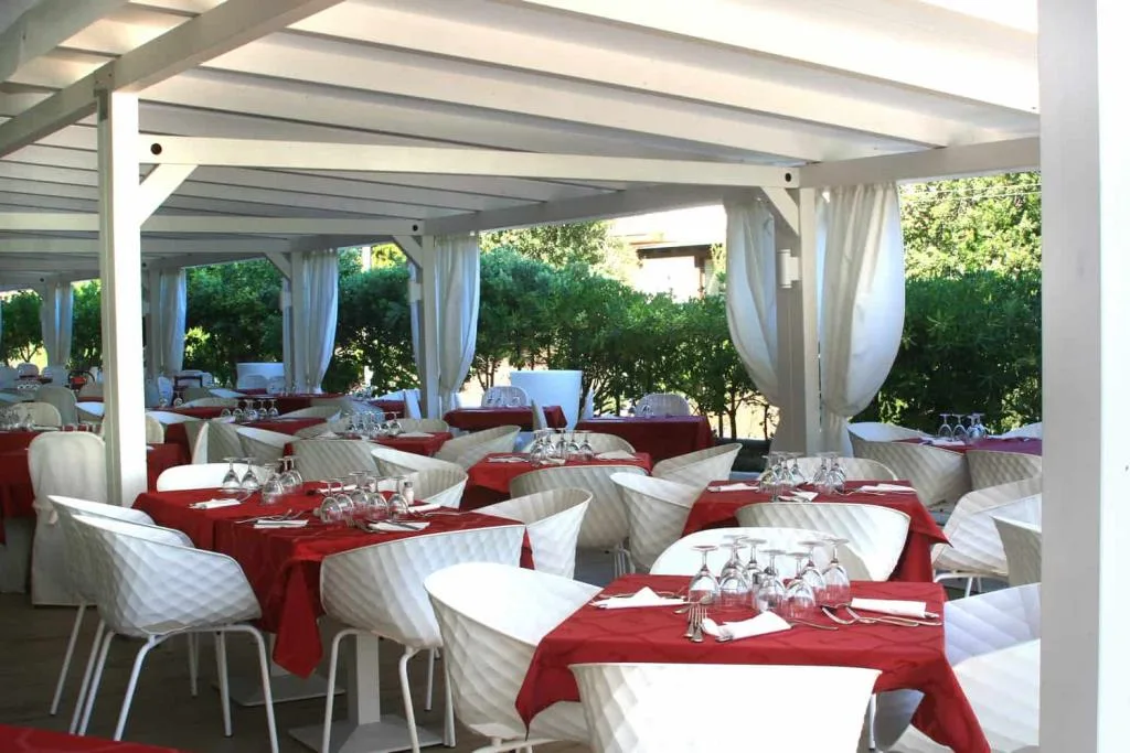 Area pranzo esterna con pergolato bianco, tavoli con tovaglie rosse e sedie moderne