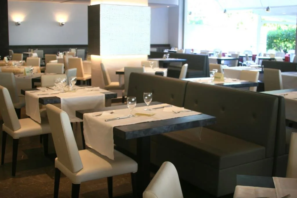 Sala ristorante interna elegante con tavoli apparecchiati, sedie bianche e divanetti