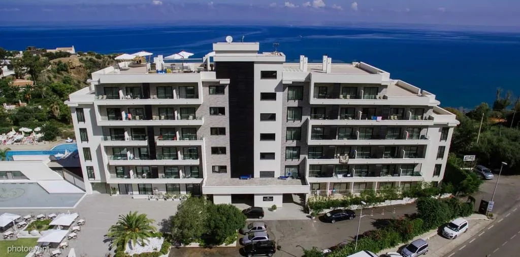 Vista aerea dell'hotel bianco fronte mare con piscina e giardini