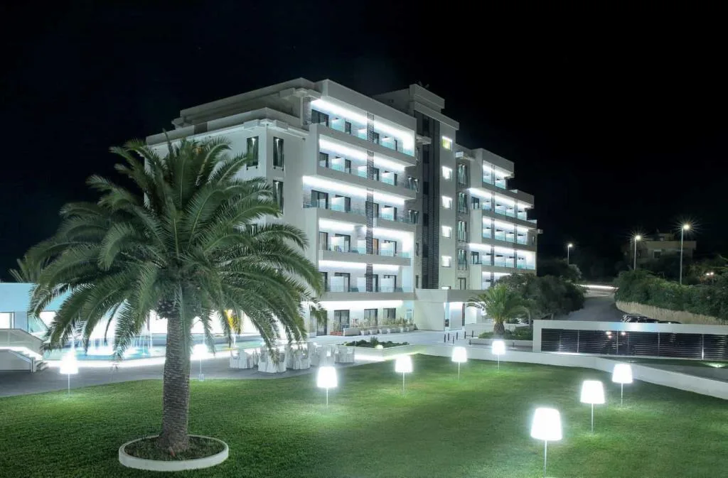 Facciata dell'hotel illuminata di notte con palma e giardino con lampade a terra