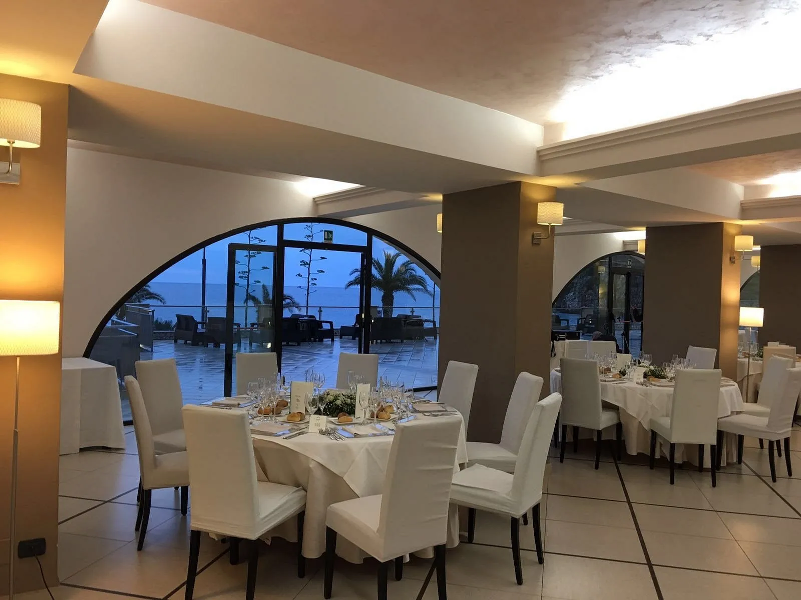 Sala ristorante elegante con tavoli rotondi apparecchiati e vista sul mare