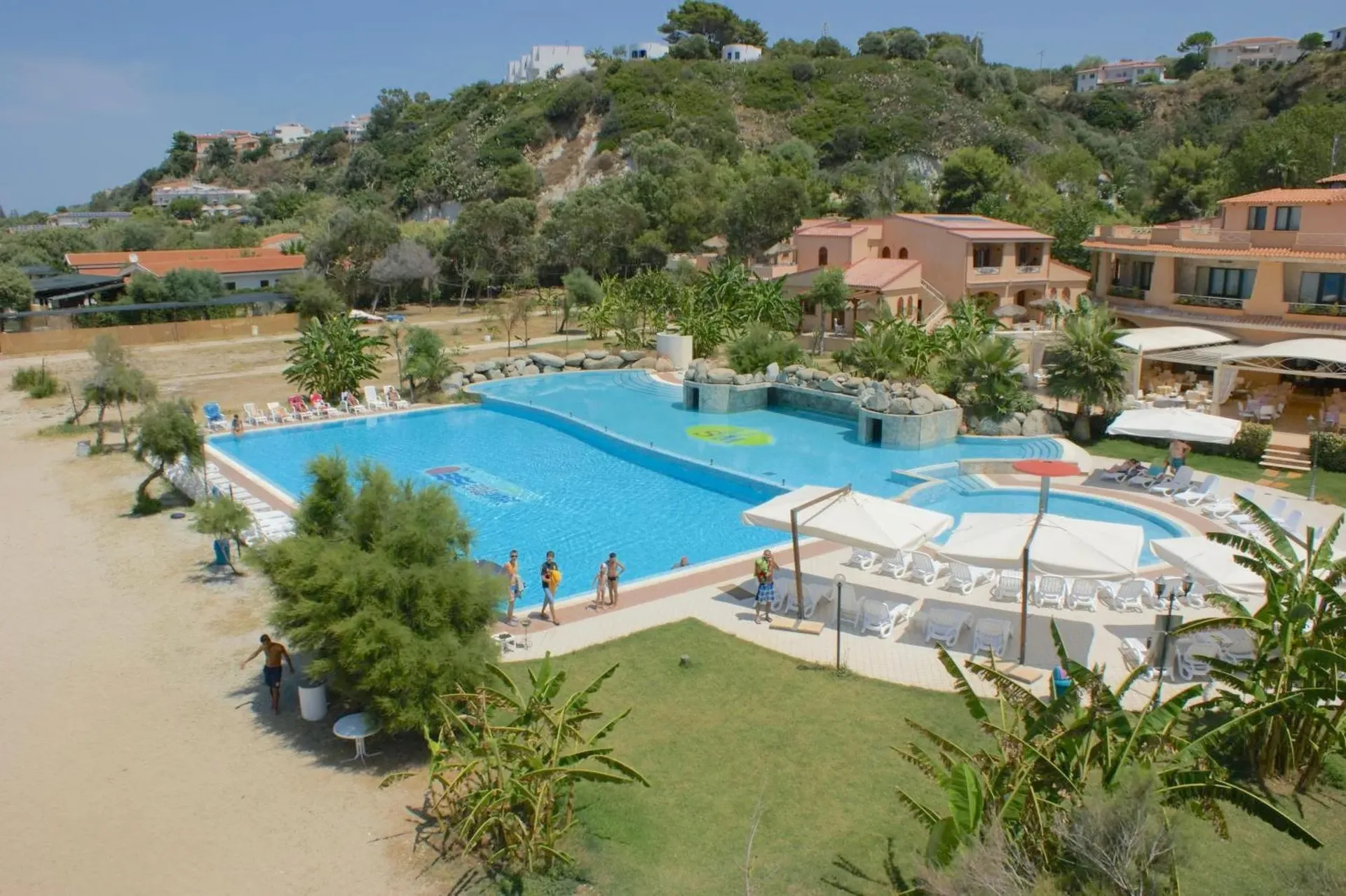 Vista panoramica del resort con grande piscina, lettini e vegetazione tropicale