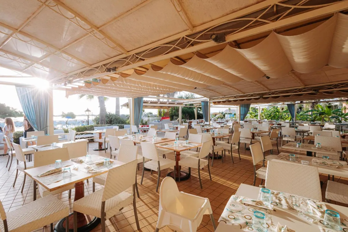 Ristorante all'aperto coperto da tende con tavoli e sedie bianche apparecchiati