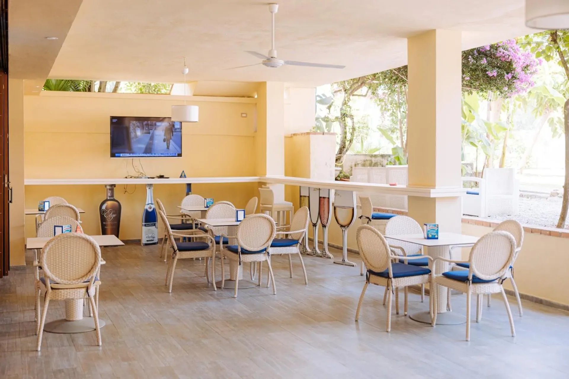 Area bar interna con tavoli, sedie in vimini e divani affacciata sul giardino