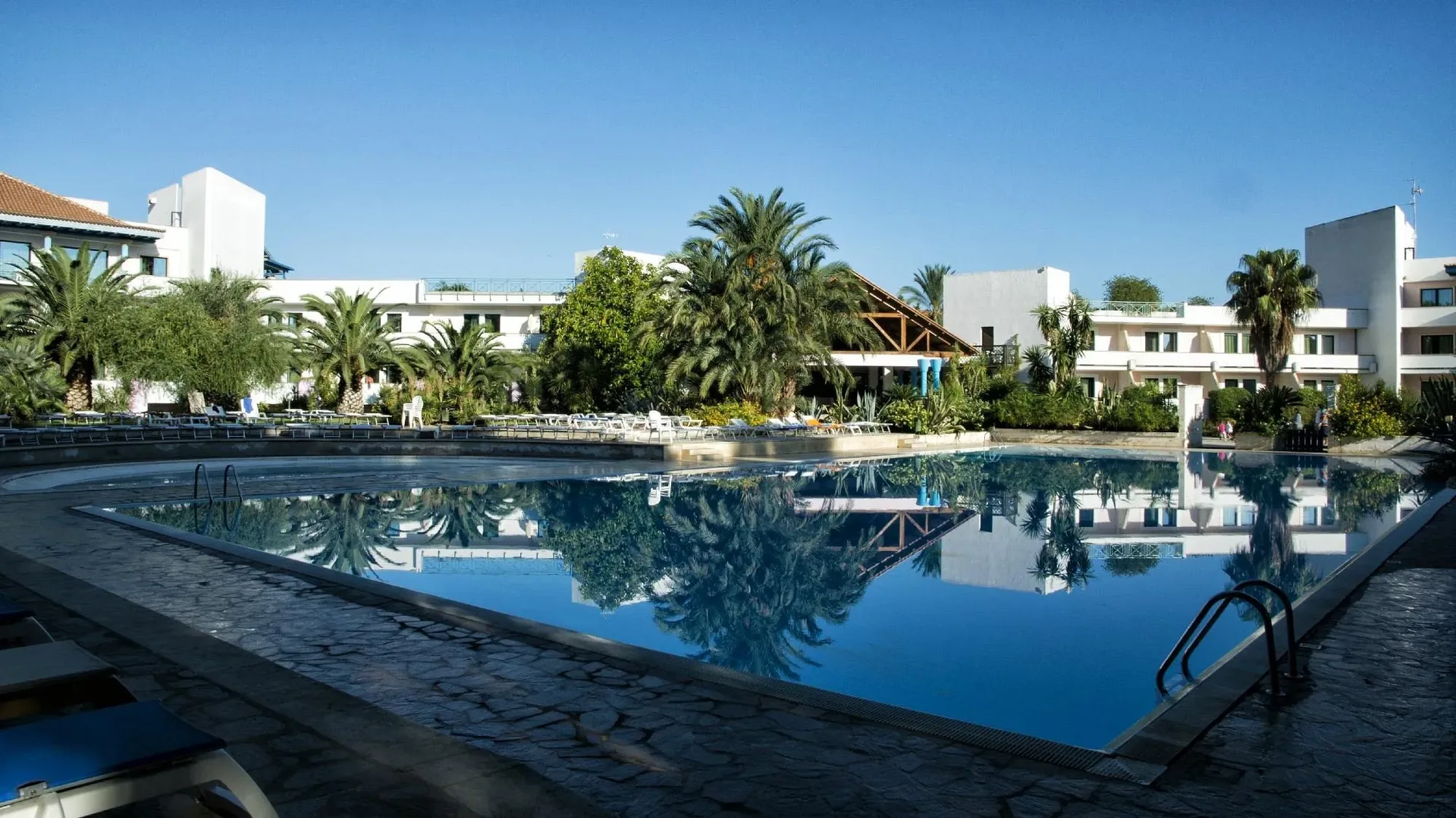 Grande piscina che riflette le palme circondata dagli edifici bianchi del resort