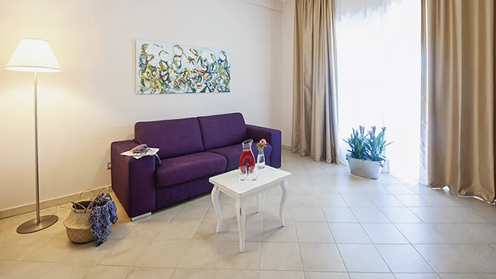 Zona soggiorno con divano viola, tavolino bianco e quadro colorato