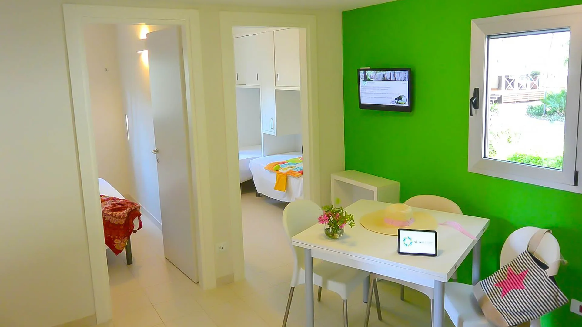 Soggiorno con parete verde, tavolo da pranzo e TV, camere adiacenti