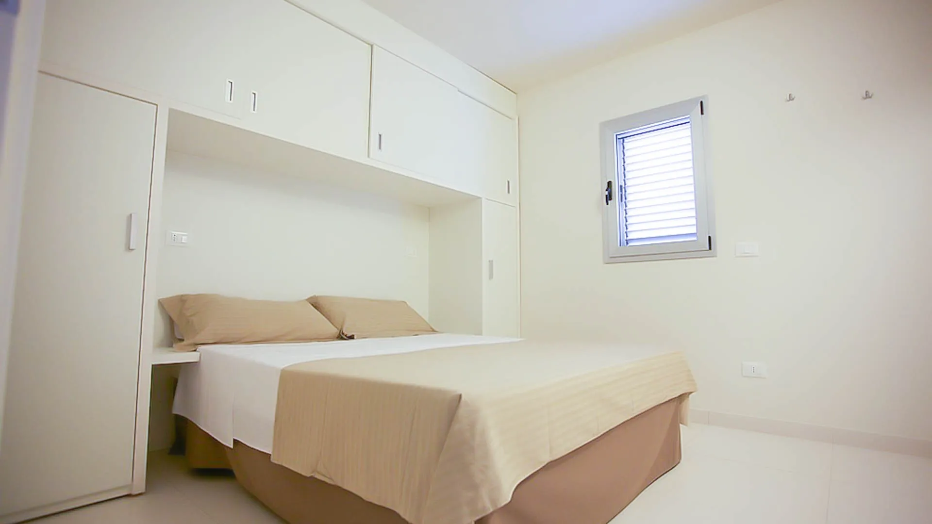 Camera da letto matrimoniale con armadiature bianche e piccola finestra