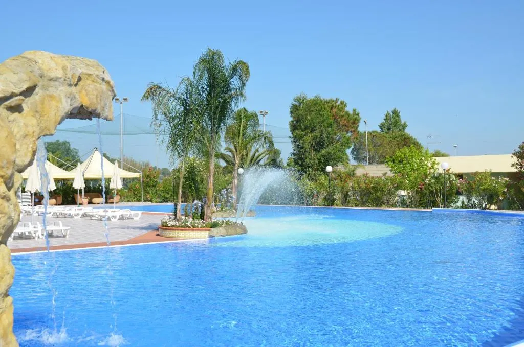 Piscina con fontana centrale e cascata rocciosa tra palme e fiori