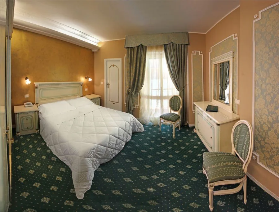 Camera classica con pareti beige, moquette verde a motivi e tende eleganti alla finestra