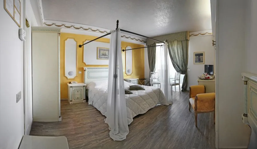Camera matrimoniale con letto a baldacchino, pareti gialle decorate e pavimento in legno