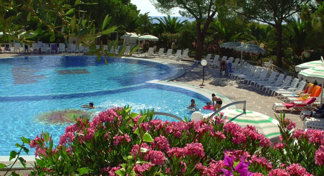 Piscina immersa nel verde con fiori rosa e ospiti in acqua