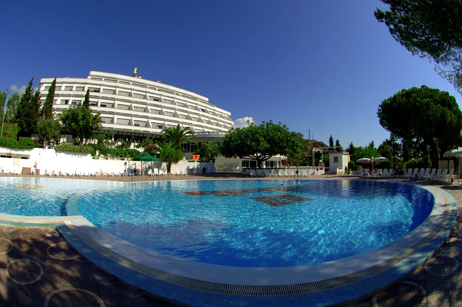 Grande piscina esterna con la facciata bianca dell'hotel e cielo azzurro