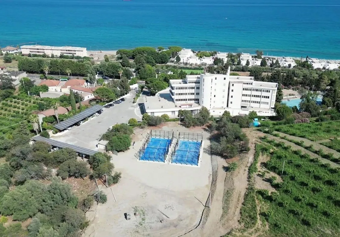 Vista aerea dell'hotel con campi da padel, parcheggio coperto e mare