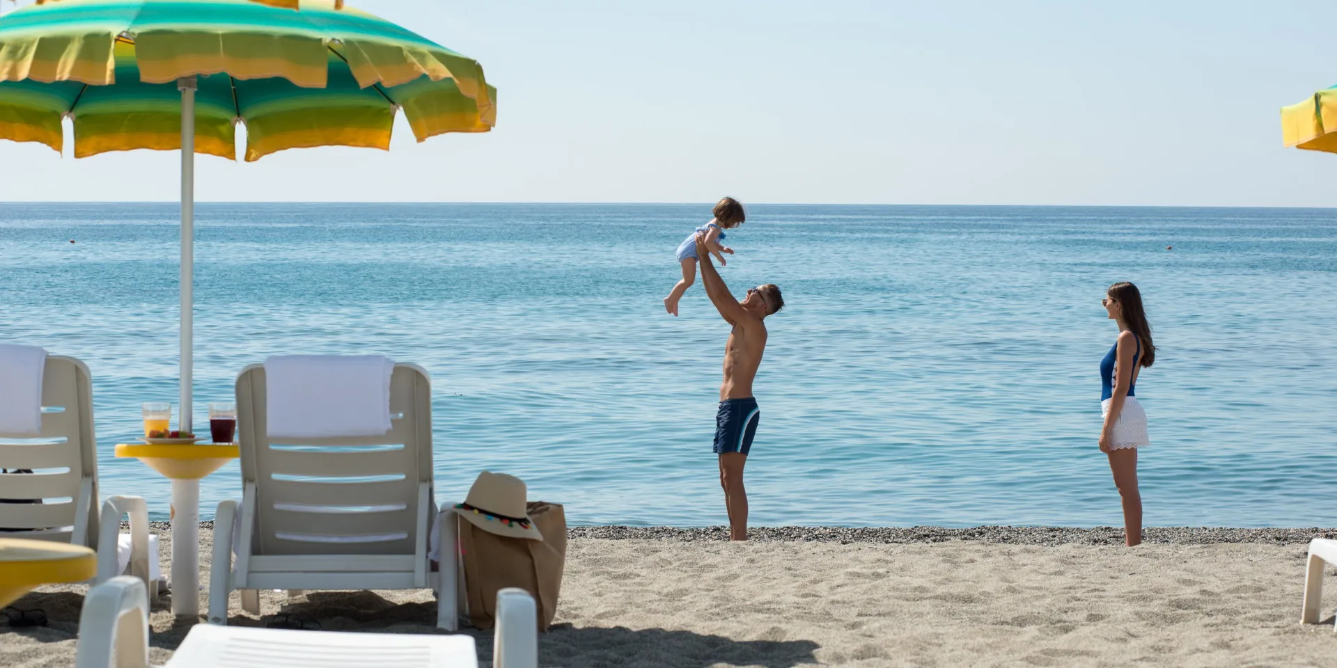 Famiglia gioca in spiaggia accanto a lettini e ombrellone con vista sul mare