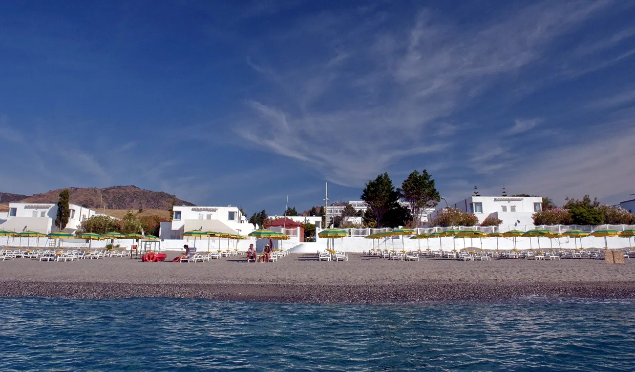 Spiaggia di sabbia con ombrelloni gialli e verdi e villette bianche