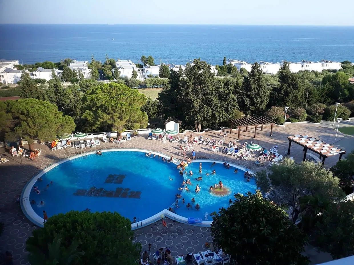 Vista dall'alto della piscina del resort con ospiti e mare sullo sfondo