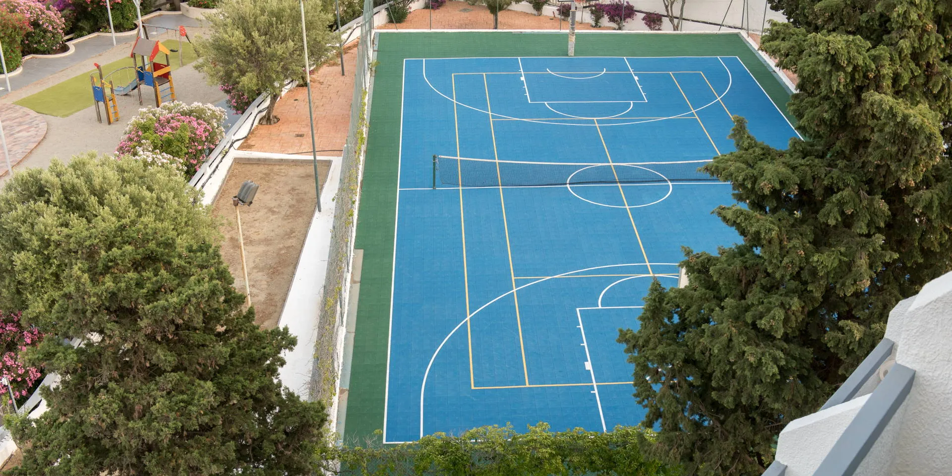 Campo polivalente blu con area giochi per bambini circondato dal verde