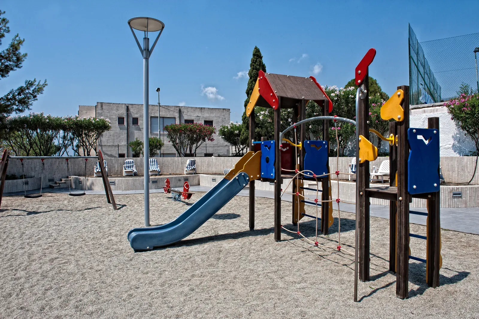Area giochi per bambini con scivolo e altalene su superficie sabbiosa