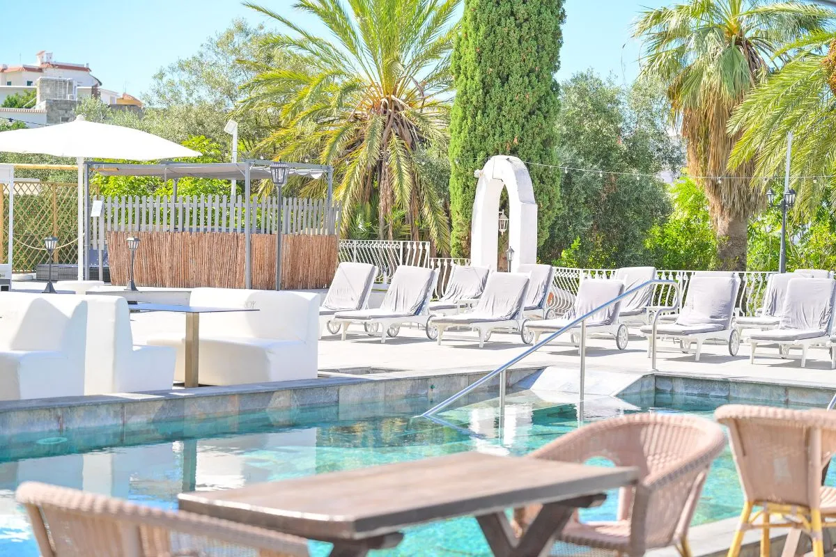 Bordo piscina con lettini, divanetti bianchi e vegetazione mediterranea