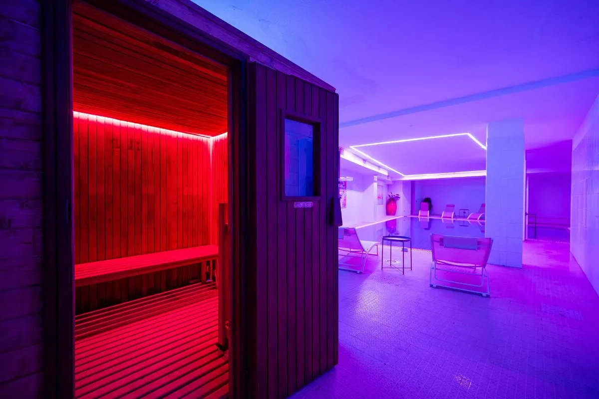 Sauna in legno con luce rossa e area relax con illuminazione viola
