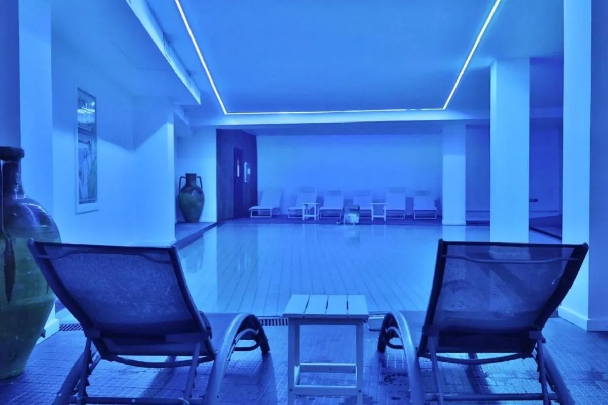 Piscina interna con luce blu e lettini relax lungo la parete