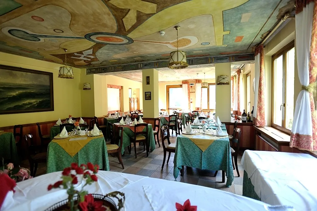 Sala da pranzo con soffitto affrescato colorato, tavoli eleganti e tende chiare