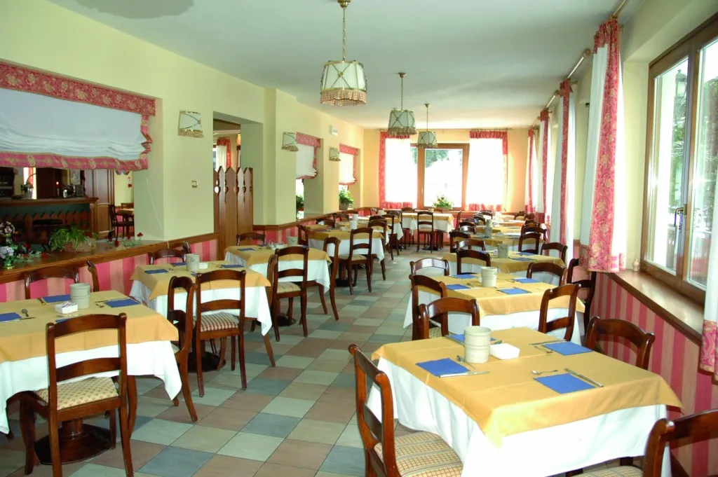 Sala ristorante con tavoli apparecchiati, tovaglie gialle e tende rosa alle finestre