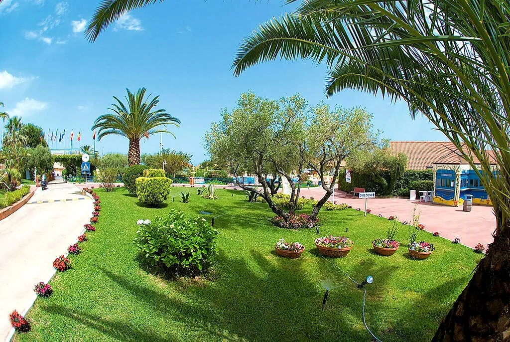 Giardino curato con palme, aiuole fiorite e prato verde all'ingresso del resort