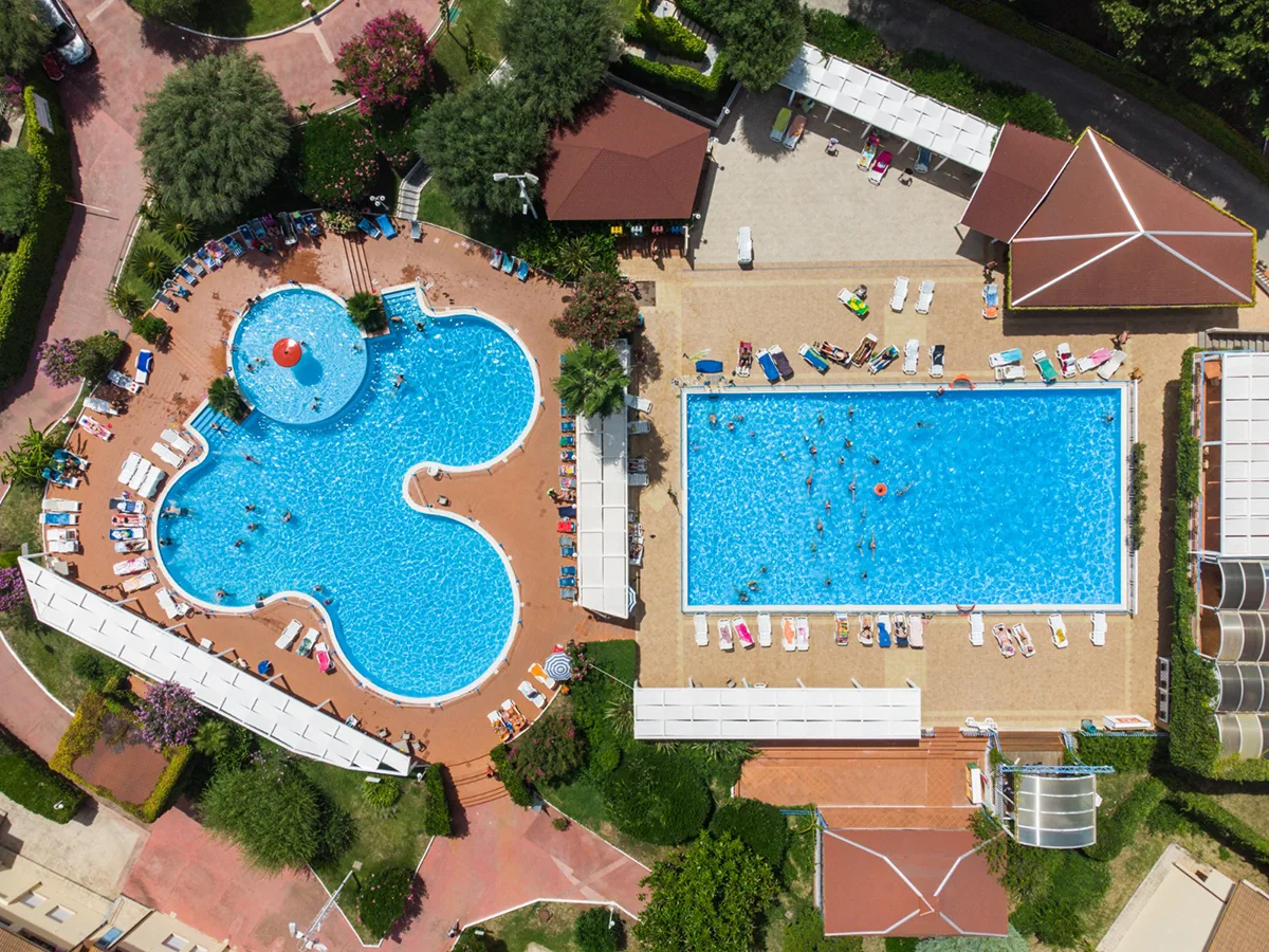 Vista aerea di due piscine, una a forma di trifoglio e una rettangolare, con lettini