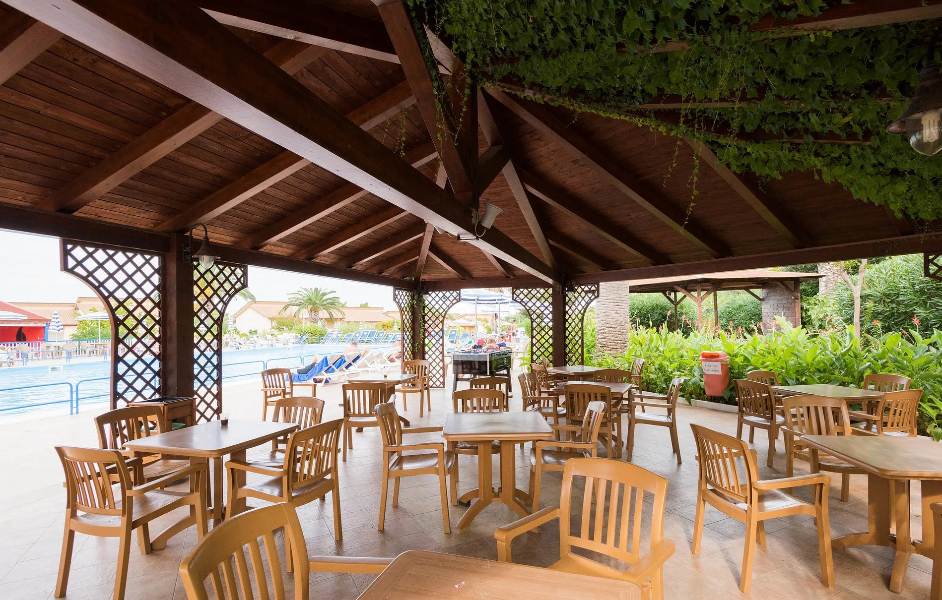 Area bar coperta con struttura in legno, tavoli e sedie affacciata sulla piscina