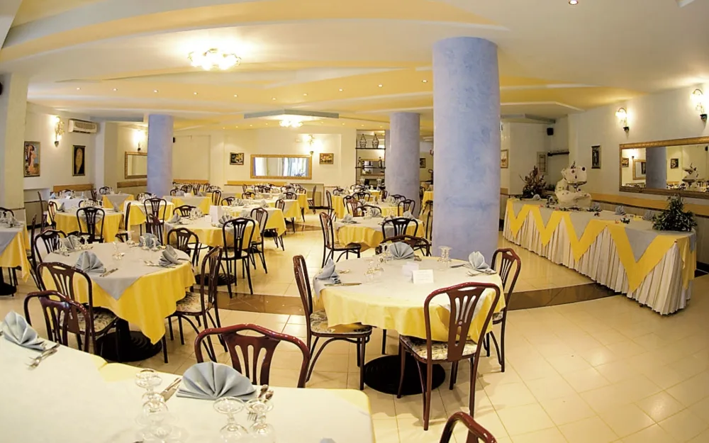 Sala ristorante interna con tavoli apparecchiati, tovaglie gialle e colonne