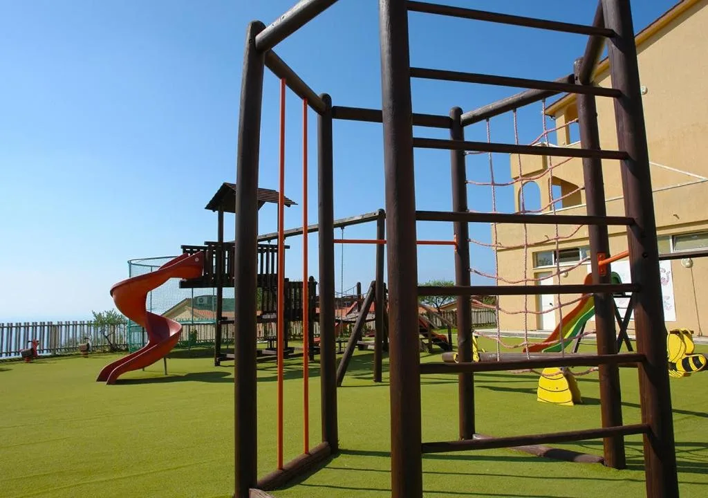 Parco giochi per bambini con arrampicata, scivolo e altalene su prato sintetico