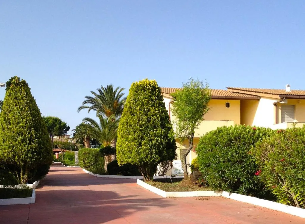 Vialetto pedonale del villaggio con siepi curate, palme e villette gialle