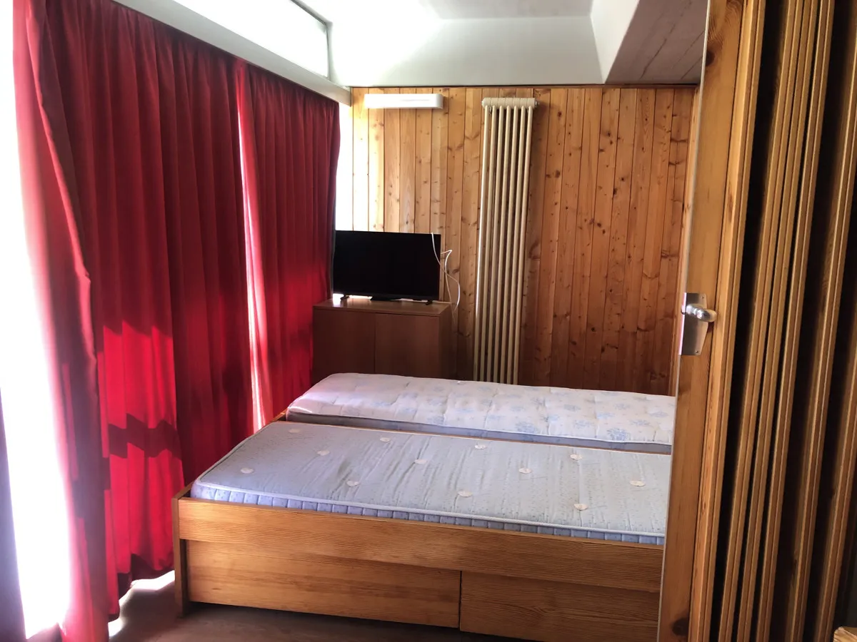 Camera da letto matrimoniale con pareti in legno, tende rosse, TV e termosifone