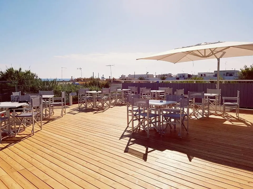 Terrazza in legno con tavoli, sedie e ombrellone bianco con vista sul mare
