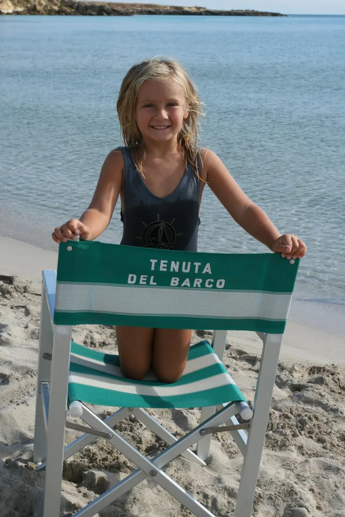 Bambina sorridente con sedia da spiaggia Tenuta del Barco in riva al mare