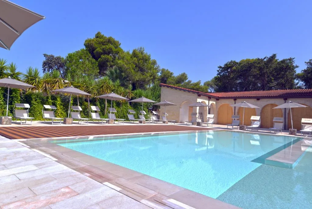 Piscina con lettini e ombrelloni grigi accanto a edificio in pietra con archi