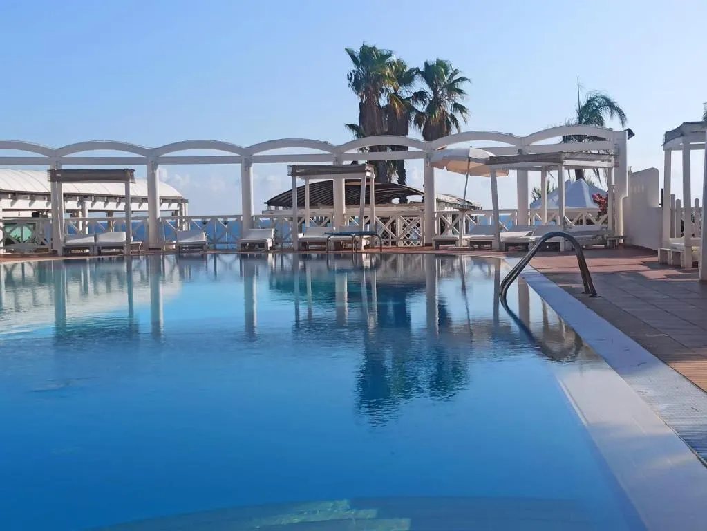 Piscina con acqua azzurra, gazebo bianchi e palme con vista mare