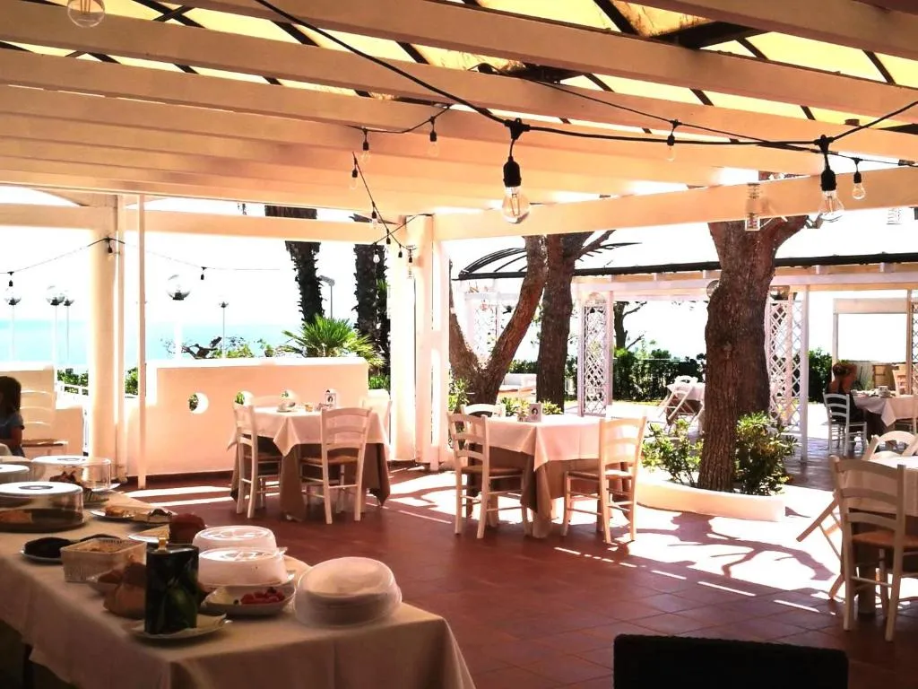 Sala ristorante sotto pergolato con tavoli apparecchiati e vista mare