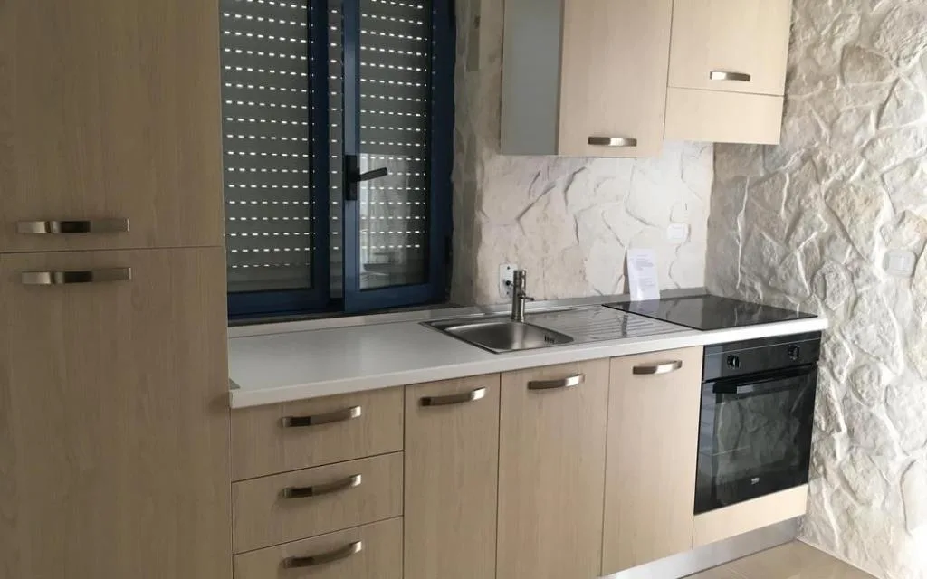 Cucina con mobili in legno chiaro, piano cottura e parete in pietra