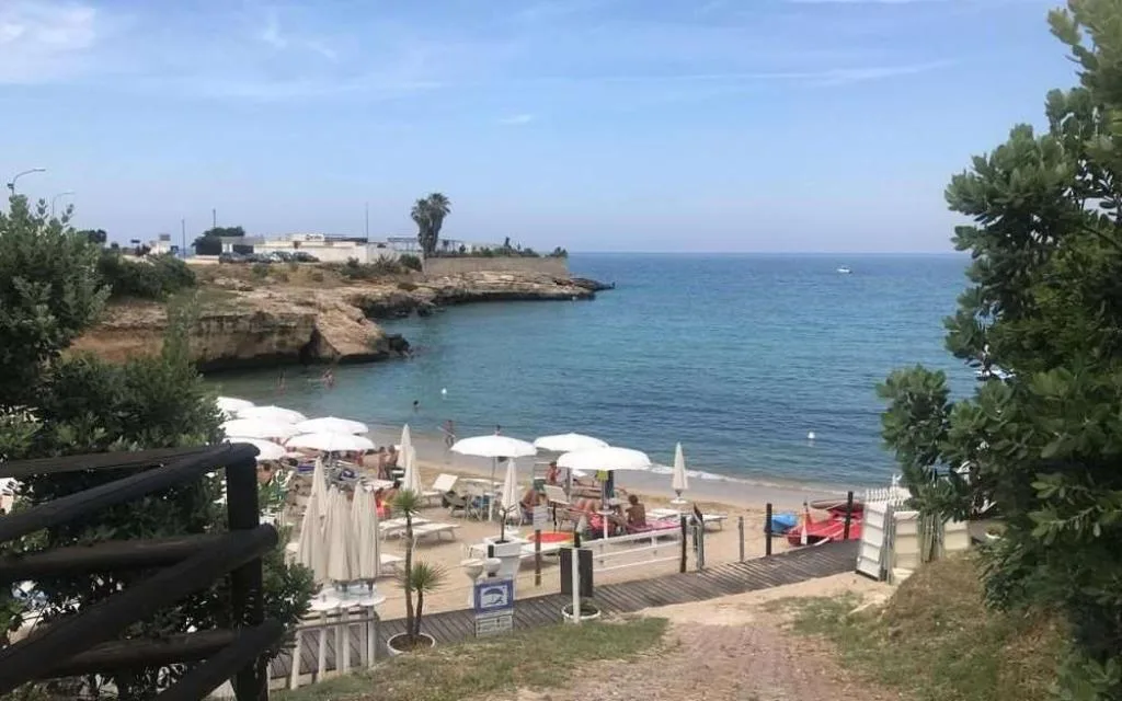 Spiaggia con lettini e ombrelloni bianchi affacciata sul mare azzurro
