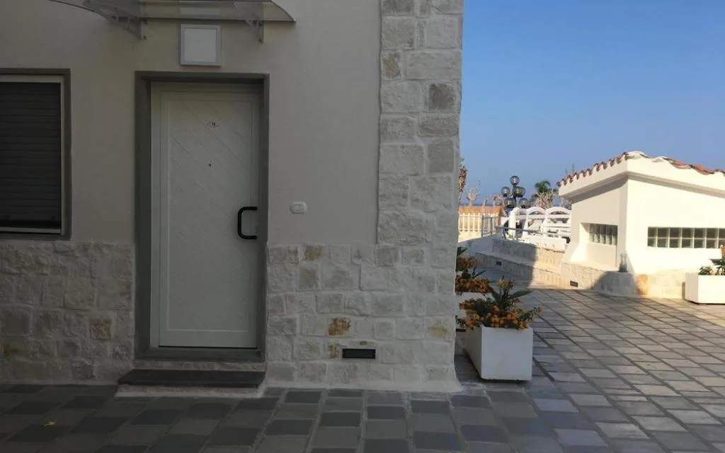 Ingresso esterno con porta bianca, rivestimento in pietra e fioriere