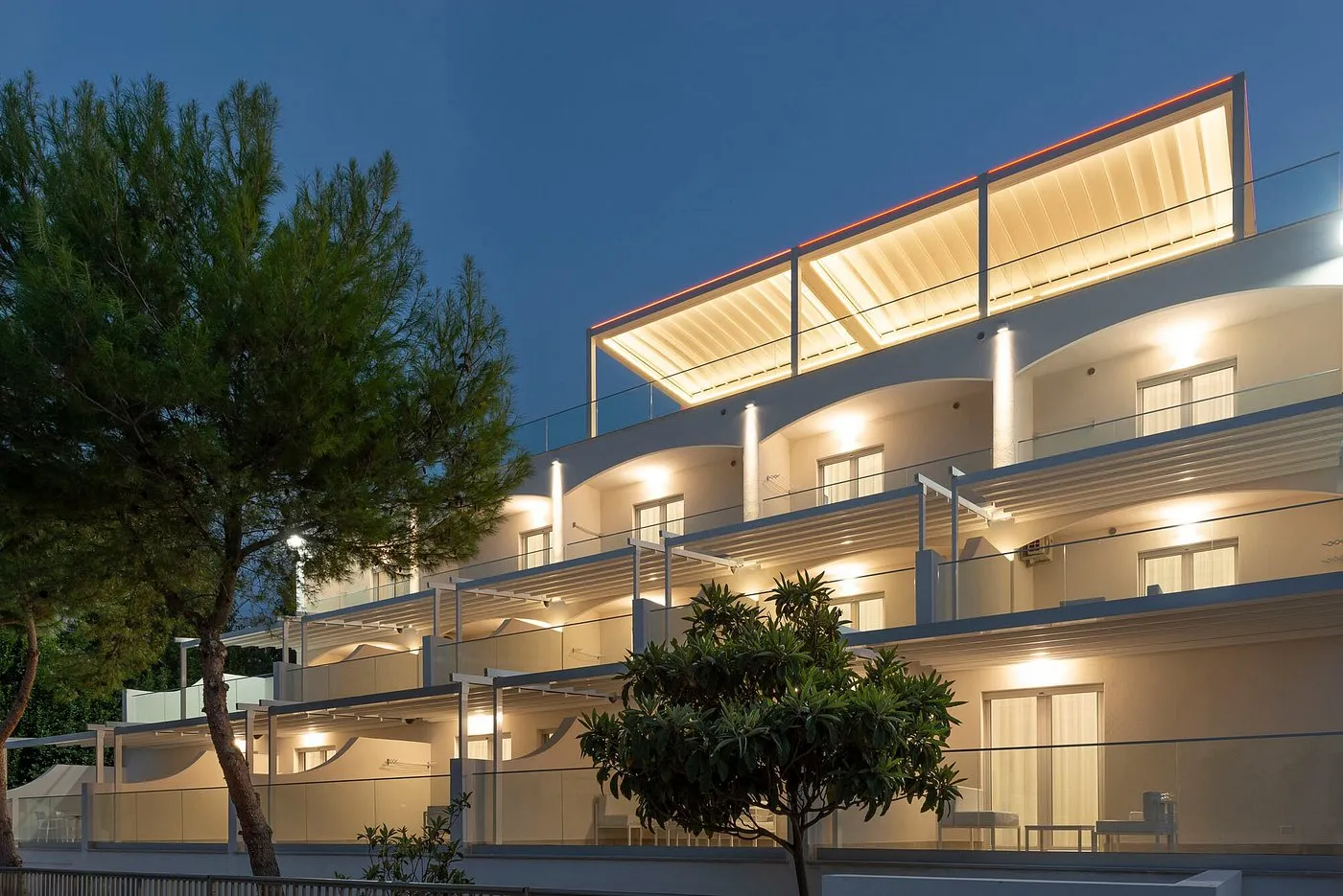 Facciata dell'hotel illuminata al crepuscolo con balconi e terrazza panoramica