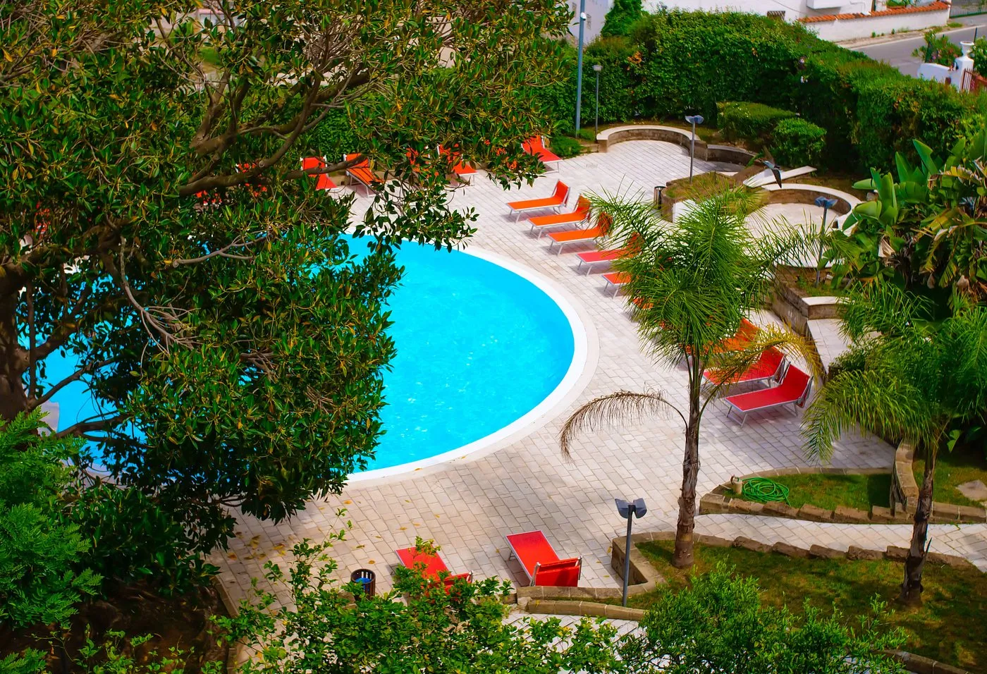 Piscina rotonda con lettini rossi e arancioni vista dall'alto tra gli alberi