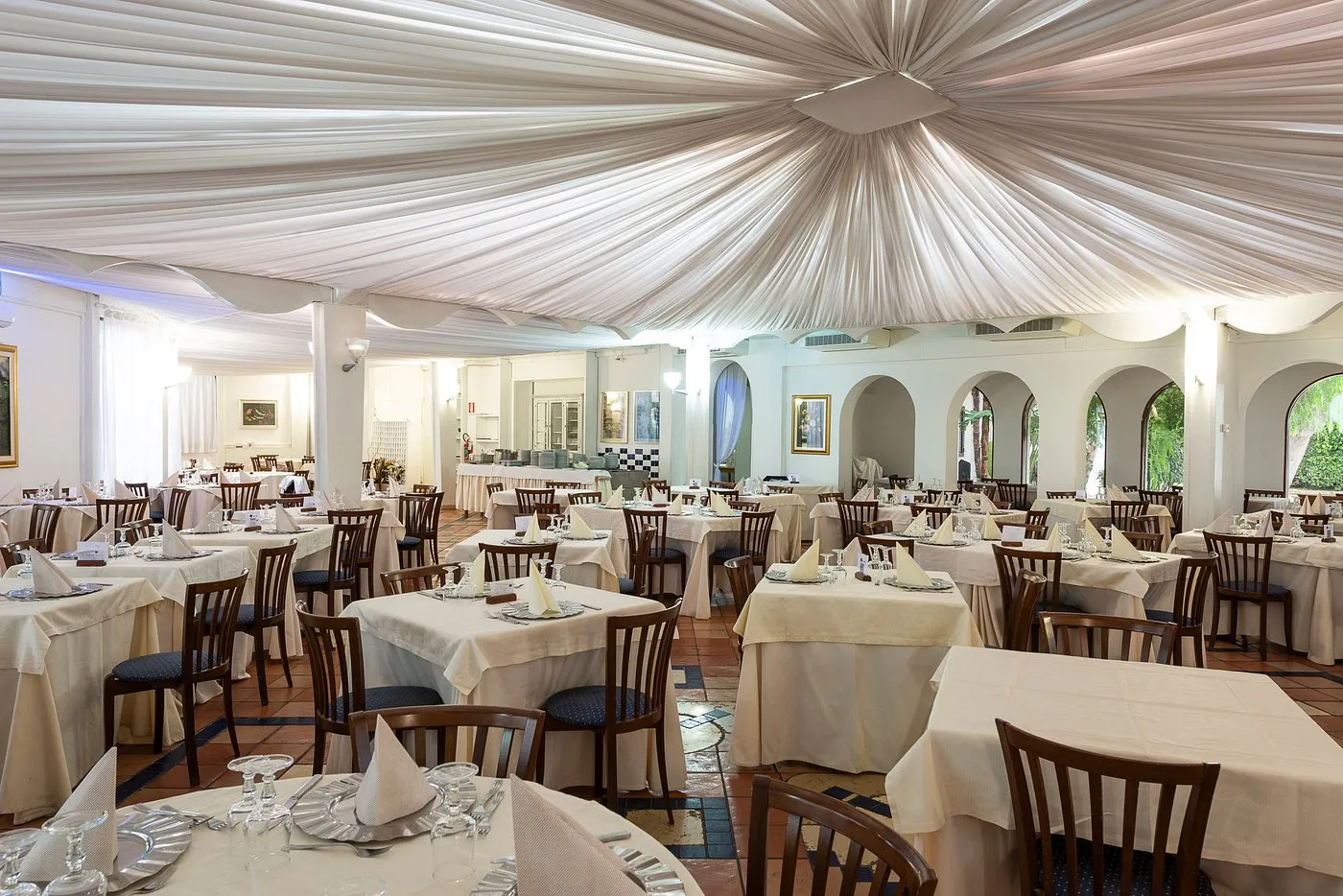 Sala ristorante interna con drappeggi bianchi al soffitto e tavoli apparecchiati